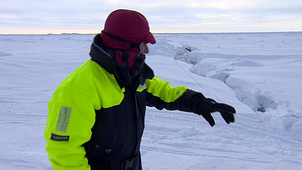 BBC science editor David Shukman stands next to a large crack in the Arctic ice