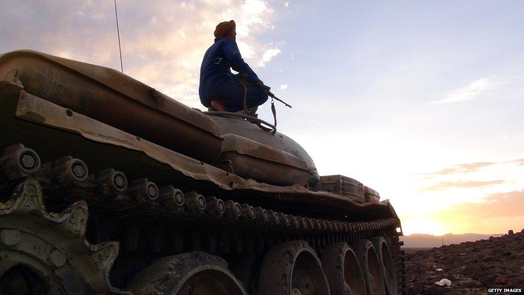 An armed Yemeni tribesman sits on a tank.