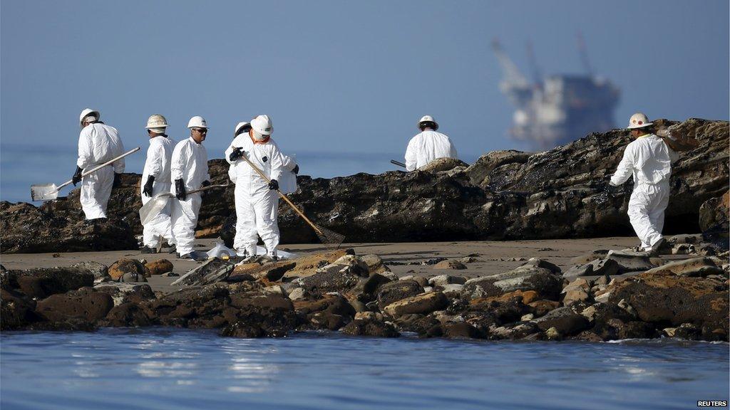 Workers on a beach with an oil platform in the background