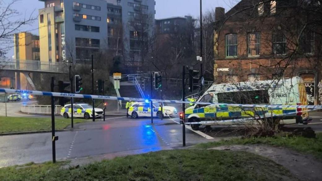 Three police vans parked across a taped-off road.