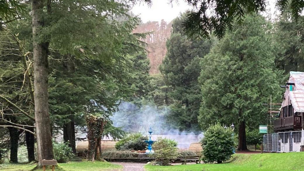 Glen Helen, which is a valleyed woodland area. There is smoke coming from an old glamping pod, and other wooded pods in the background and a building to the right.