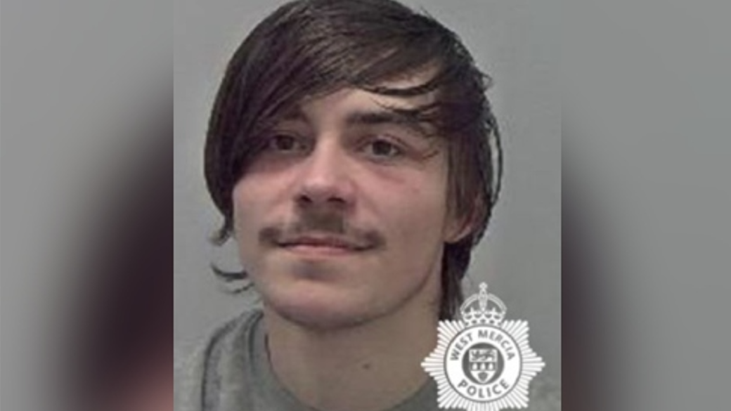 A mug shot of a man with long brown hair and a brown moustache, wearing a grey sweater