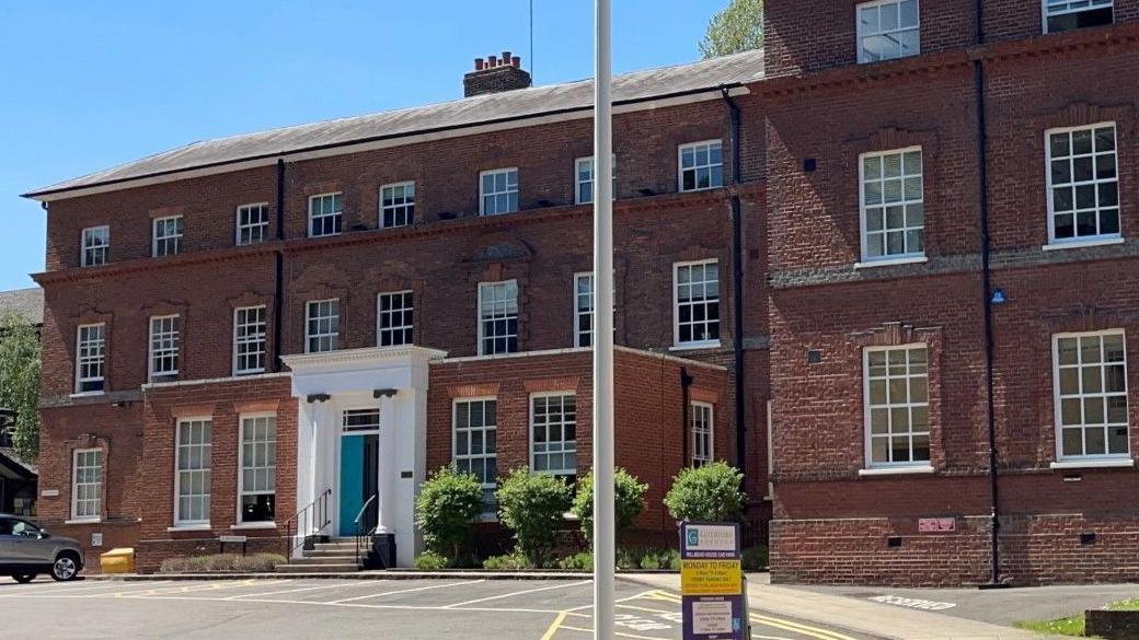 Outside Guildford Borough Council's HQ, Millmead House, in Guildford, Surrey. The three-storey building has a blue door.