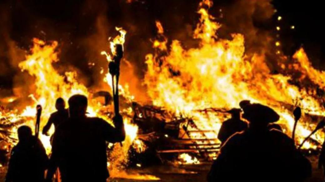 The silhouettes of people standing around a bonfire