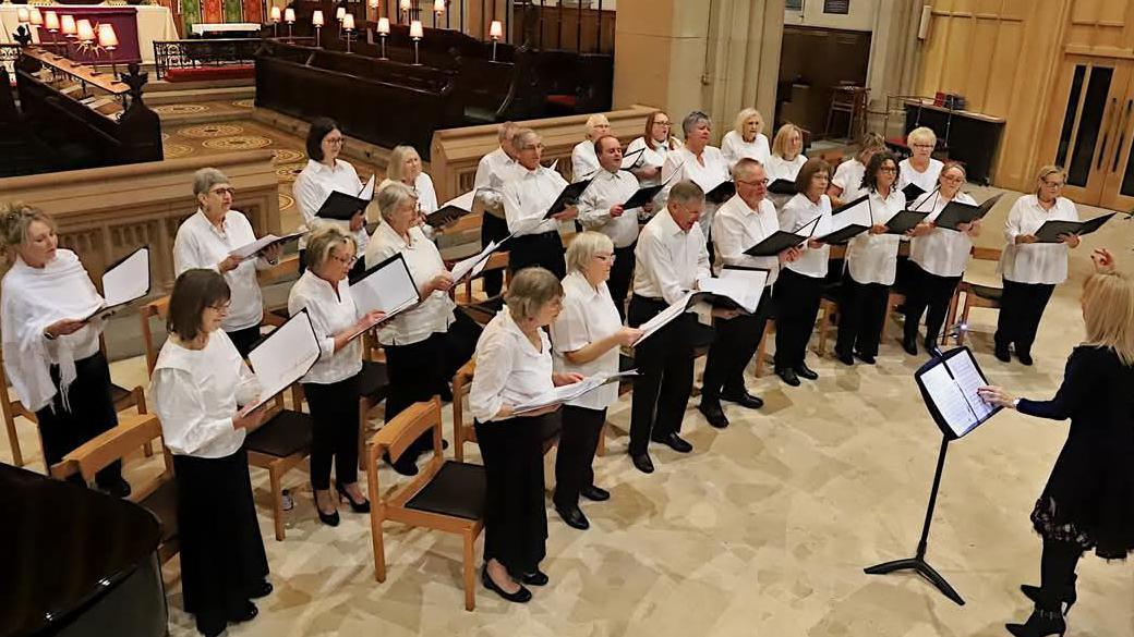 Choir members in white shirts and either black trousers or skirts sing in a church choir area