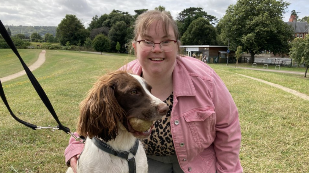 Lucy kneeling in a park with her arm around George, a springer spaniel