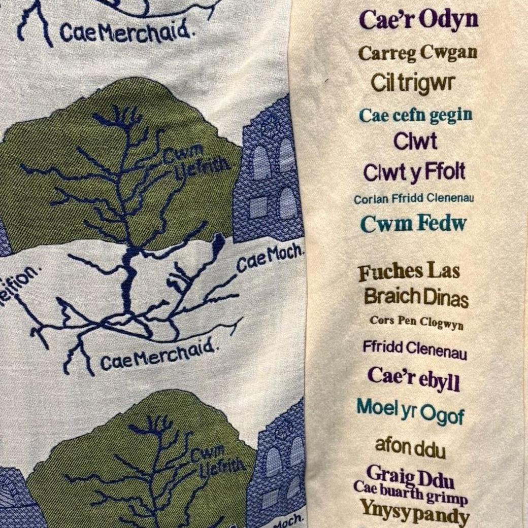 Llun o un o'r carthenni gwlan sy'n cael ei arddangos yn yr Oriel. Mae'r llun wedi ei dynnu'n agos at y carthen gyda rhestr o rai o'r enwau lleoedd i'w gweld: Bryn Weirglodd, Cwm Fedw, Fuches Las yn rhai ohonynt.