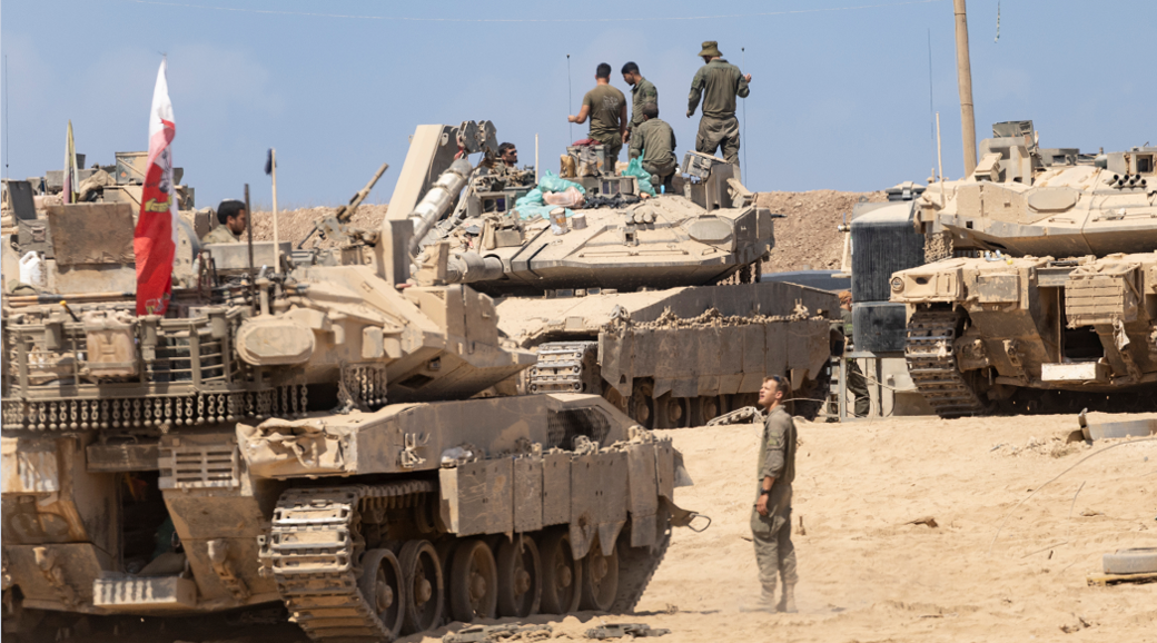 Israeli soldiers arrange equipment on several tanks in a very sandy environment.