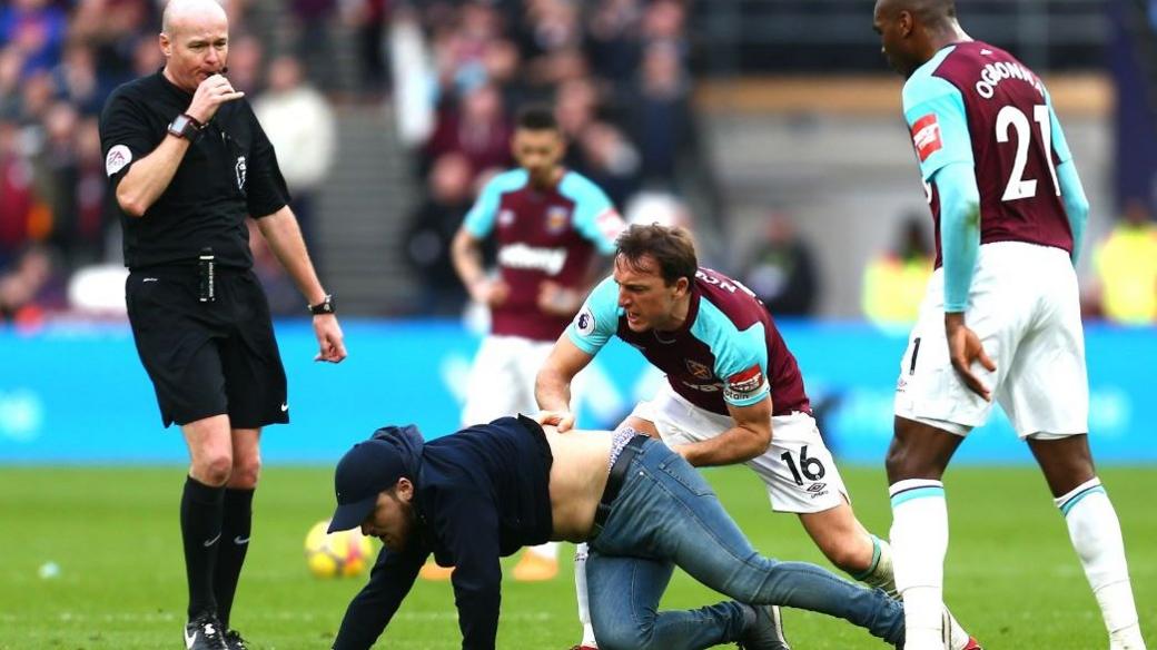 West Ham skipper Mark Noble drags a pitch invader to the floor