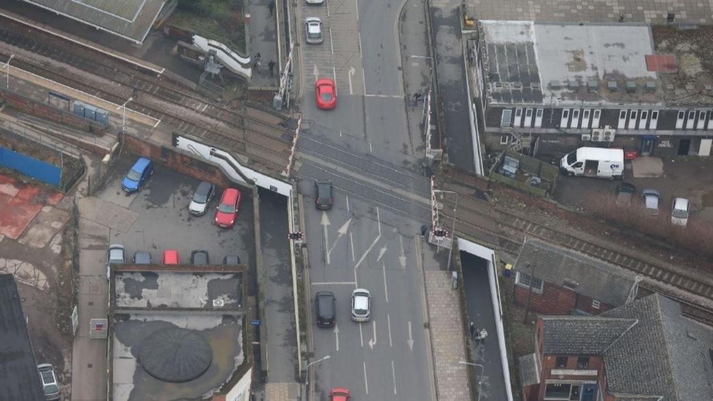 Aerial view of the railway crossing and subways. There are a number of cars on the road, along with buildings on either side.