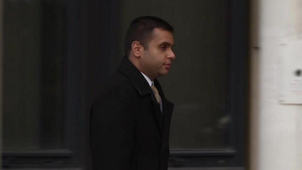 Faisal Shoukat pictured walking away from the court wearing a black overcoat and gold tie. He is carrying a briefcase.