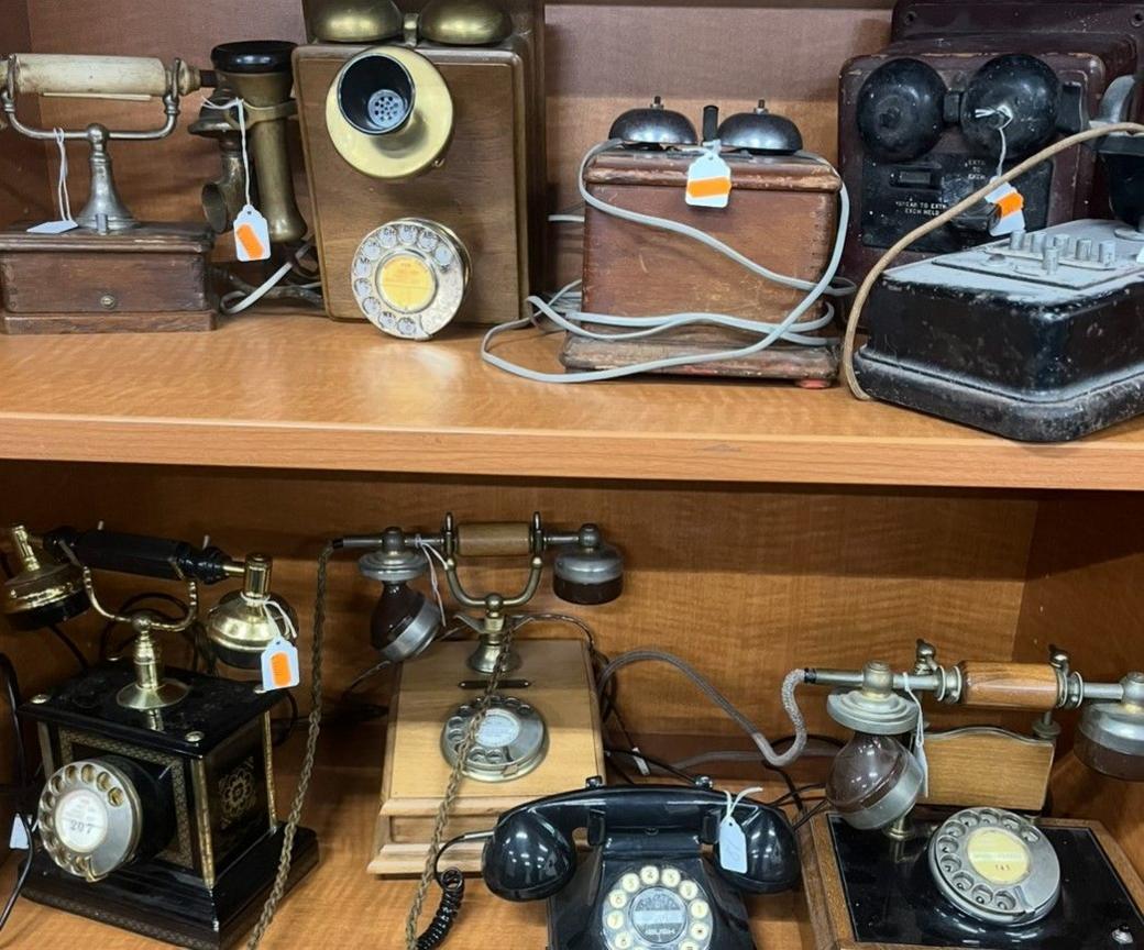 Old telephones are visible on two shelves, with four on the bottom shelf, mainly black, and a similar amount of phones on the higher shelf.