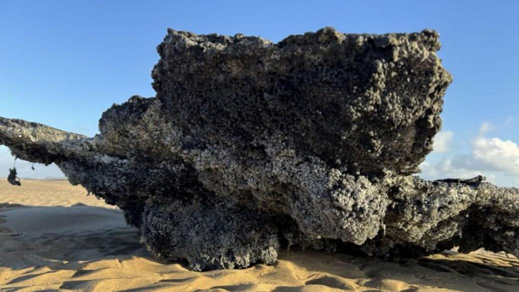 A close-up shot of burnt clump of plastic pellets on the sand.