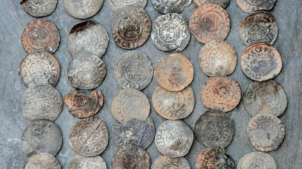 A collection of slightly corroded metal coins with medieval-style designs on them on a grey background