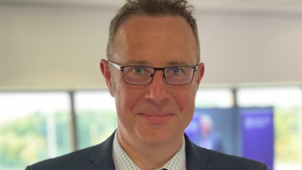 Richard Taylor, wearing a shirt, blazer jacket and glasses, looks straight ahead.