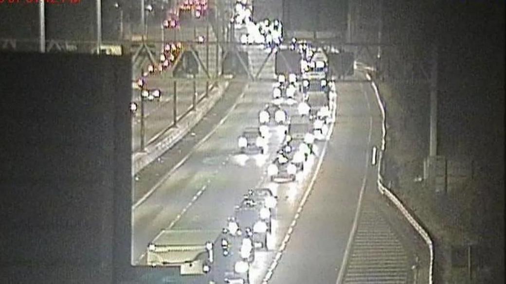 Long tailbacks of cars and lorries on two lanes of the M4 at junction 19 westbound, towards the slip road for the M5. The vehicles all have headlights on. The middle two lanes are empty.