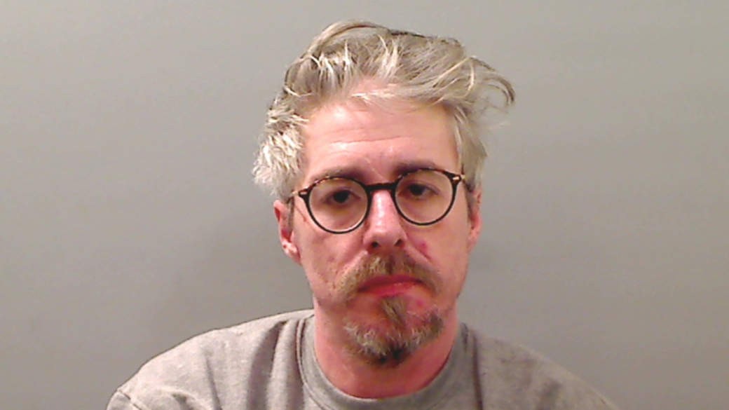 Mugshot of Barry Maguire. He has grey wavy hair and goatee, wearing glasses and a grey sweatshirt.