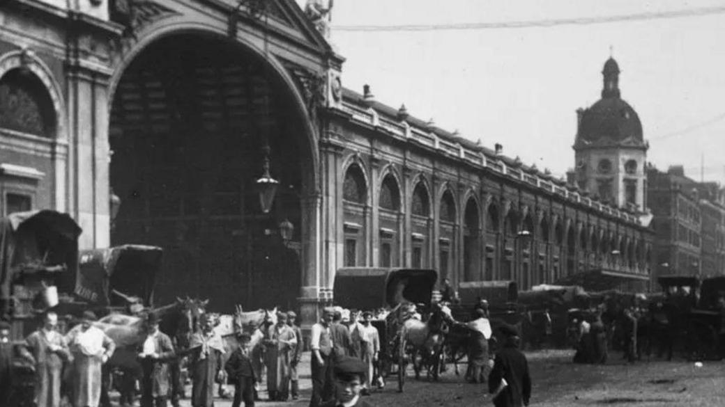 A black and white picture showing people standing outside Smithfield market 