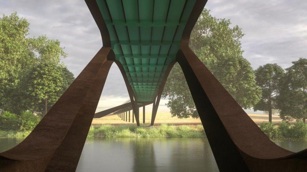 A visualised image of what the bridge could look like. The brown structure arches over the river with a green walkway. There are trees in the background and a field and the sky is full of grey clouds 