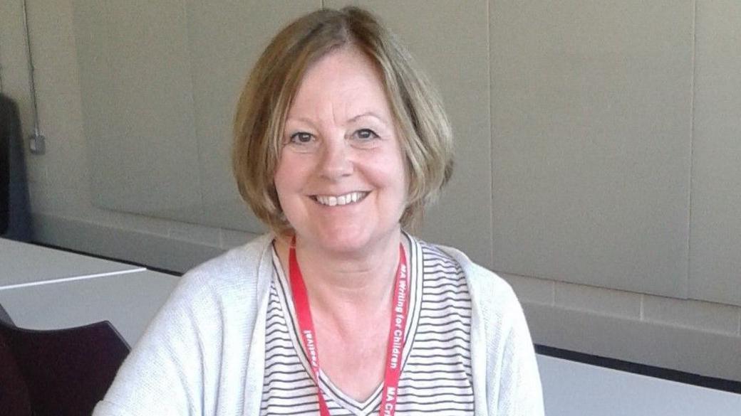 Maria McCarthy smiling at the camera and wearing a white cardigan and stripy top.