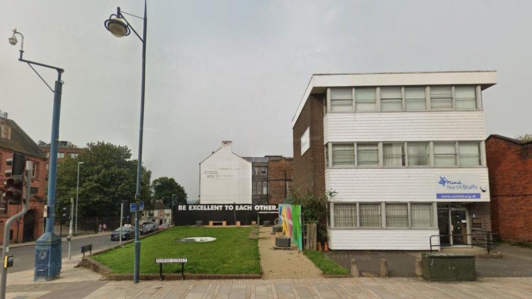 A three-storey office block with a lawned area to the side. The building is clad with white painted wooden slats.