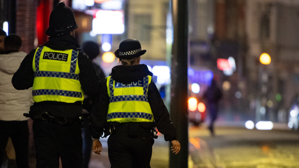 Back view of a male and female police officer walking down a Bournemouth street at night