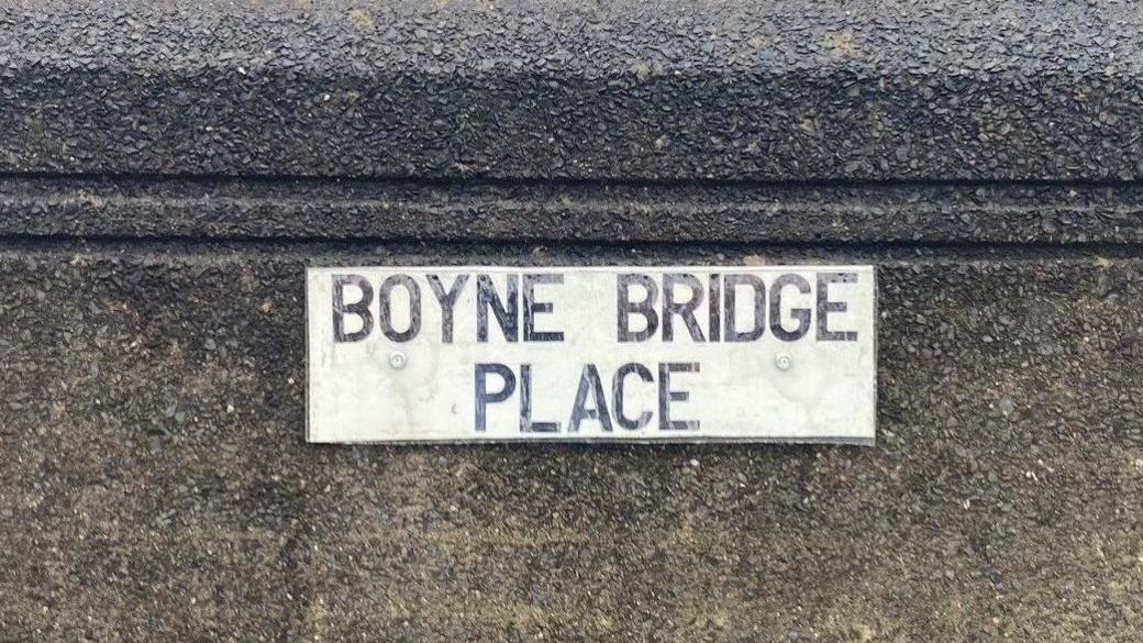 Road sign reading Boyne Bridge Place in black writing on a white background, placed on the concrete bridge