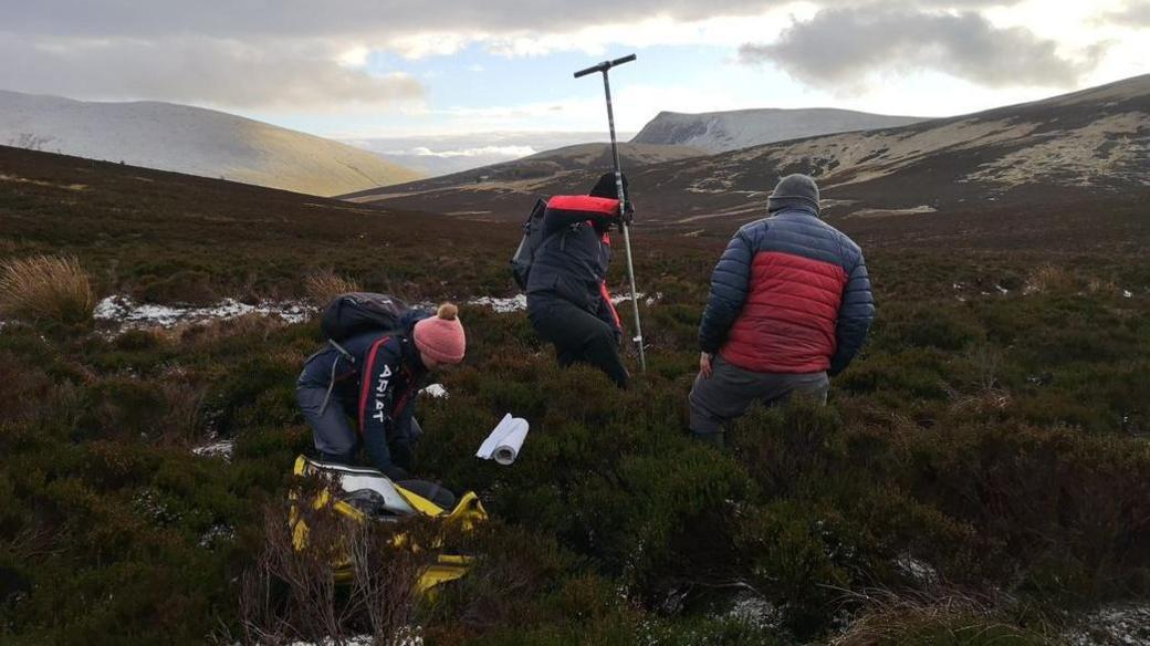 Three people using equipment to survey the peat on the lower slopes of Skiddaw.