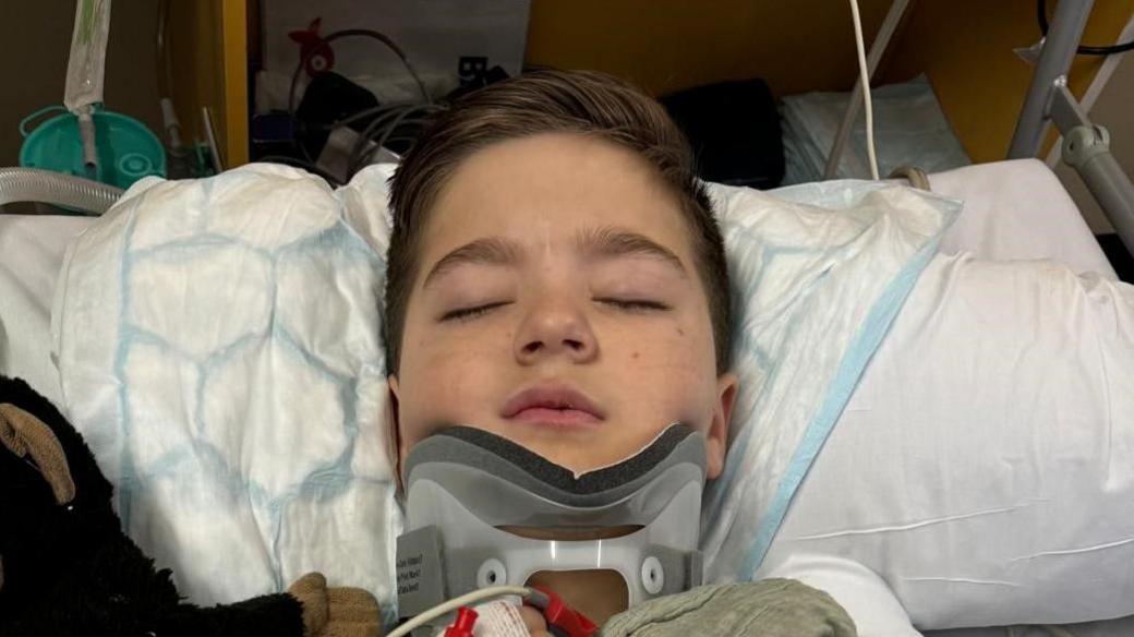 A young boy laying in a hospital bed with his eyes closed and his neck in a brace