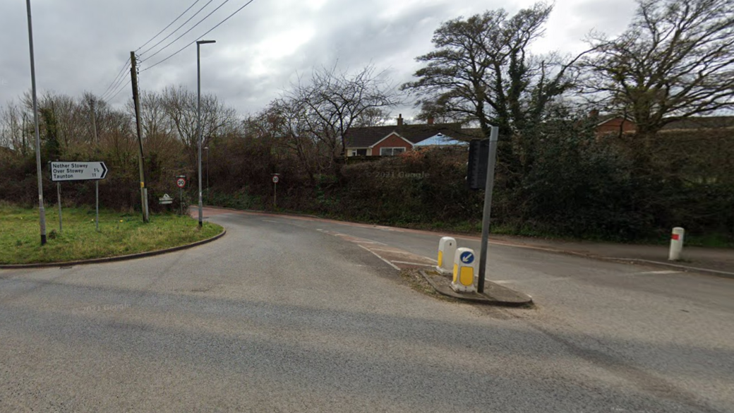 A wide Google Street View shot of the entrance to Lime Street in Nether Stowey in Somerset. There are trees either side of the junction and houses visible in the background