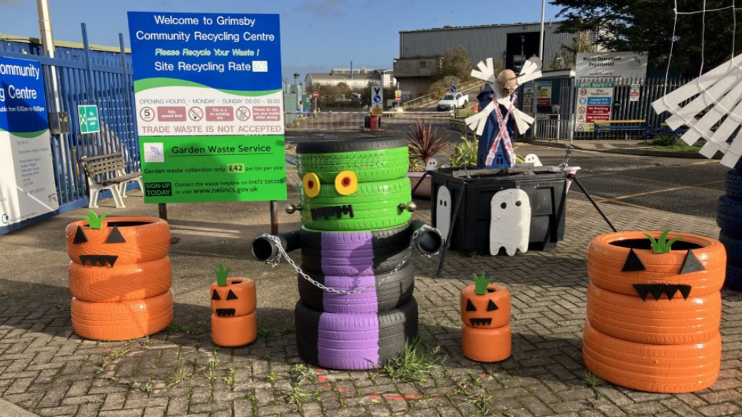 Orange tyres piled up to make halloween creatures at a community recycling centre. There are two large ones and two smaller creations. There's also a purple, black and green tyre monster.