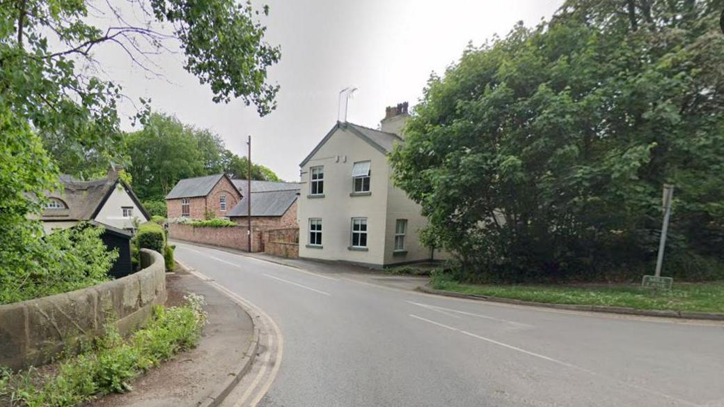 The start of Mill Lane, Mobberley, in Cheshire, showing a property with a thatched roof on the left and on the right some trees then two properties  