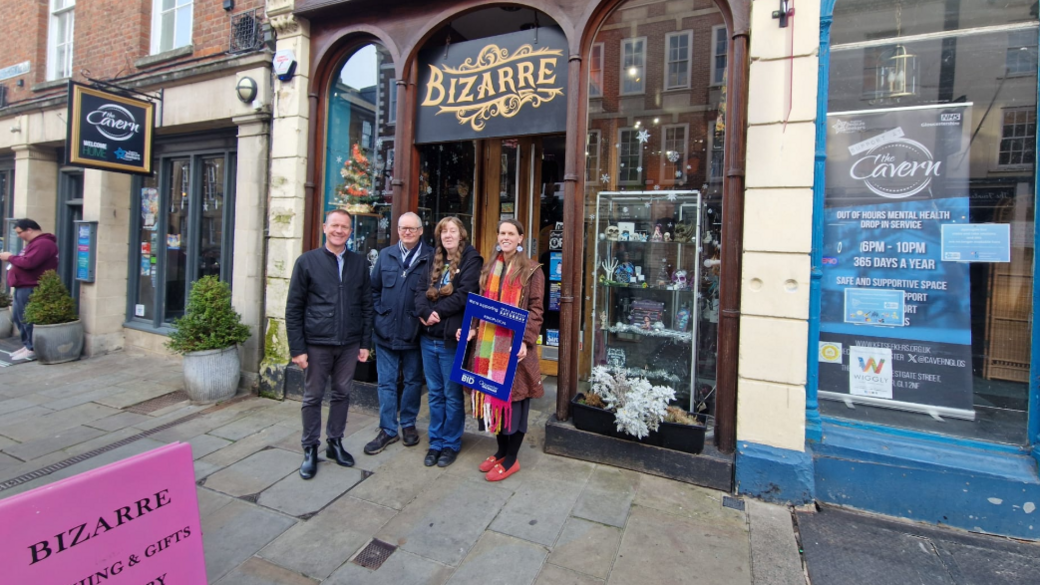 Four people standing outside a small, independent shop called Bizarre, which has small gifts, trinkets and ornaments in the window