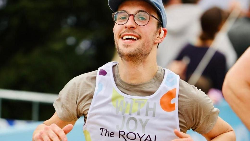 Mr Chapman is running at an event for the Royal Marsden cancer charity (and wears a t-shirt with the slogan on).  He wears a baseball cap and glasses and smiles at the camera.