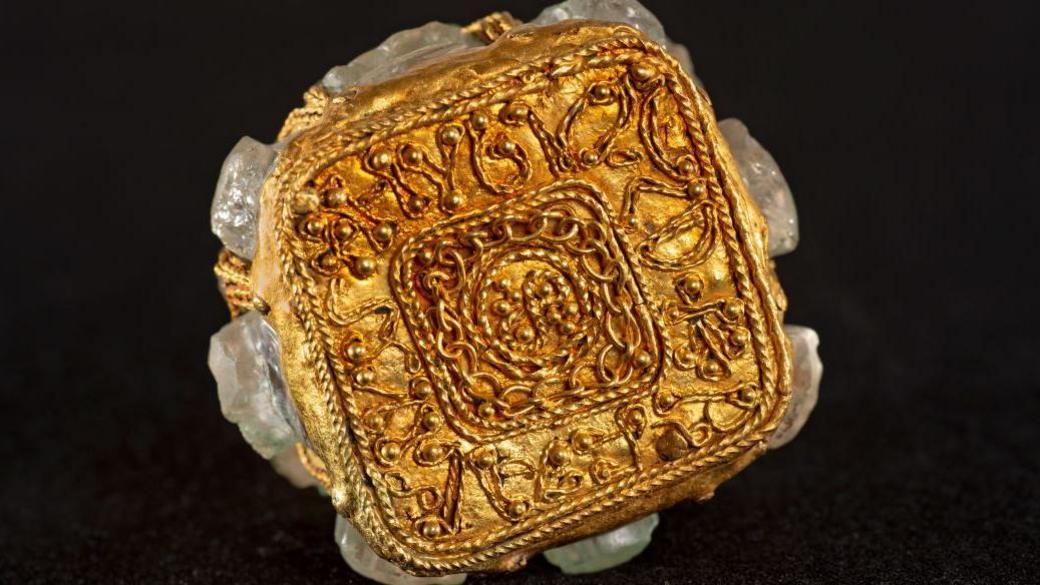 The gold inscription on the bottom of a rock crystal jar on a black background.