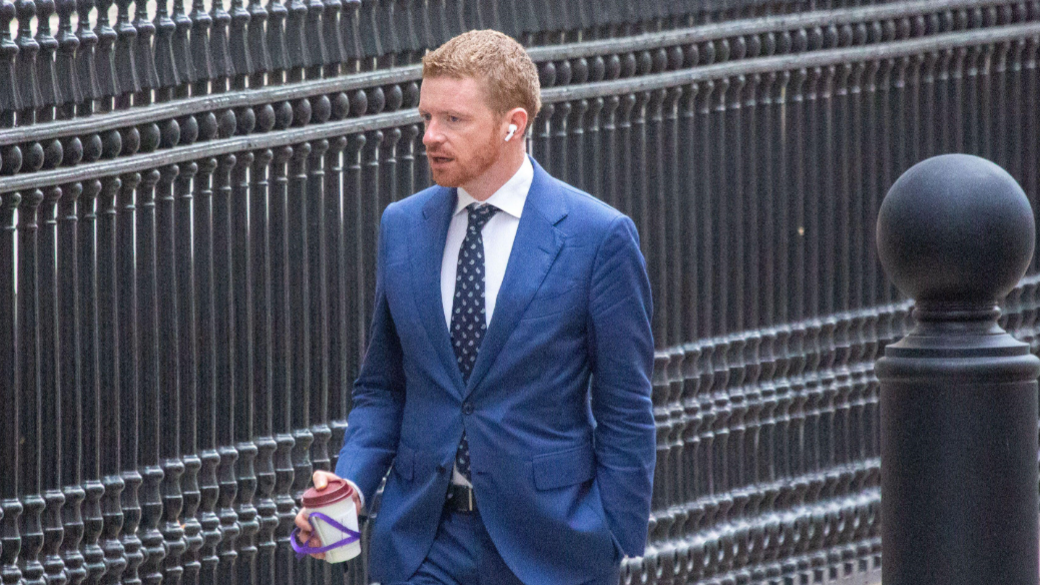 Morgan McSweeney walking up Downing Street wearing a blue suit and holding a coffee cup and wearing earpods