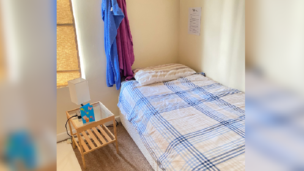 A single bed with a striped duvet cover, bedside table and lamp with cream walls. 