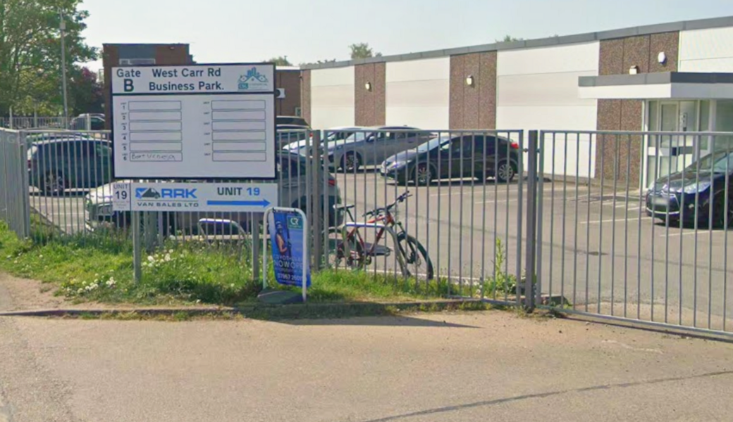 A white sign saying West Carr Rd Business Park with a grey fence behind.