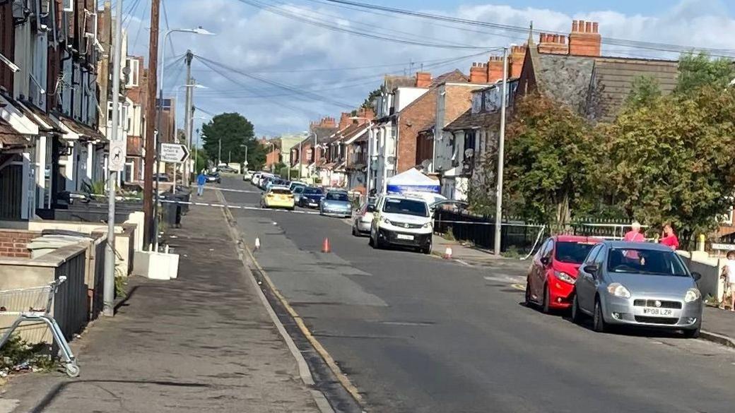 View of police car and cordon, along with other vehicles and people on Grosvenor Road in Skegness