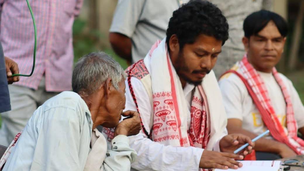 Pranab Doley seen in a white tunic with a gamusa sits and looks at some documents with a local, an old man, in Kaziranga 