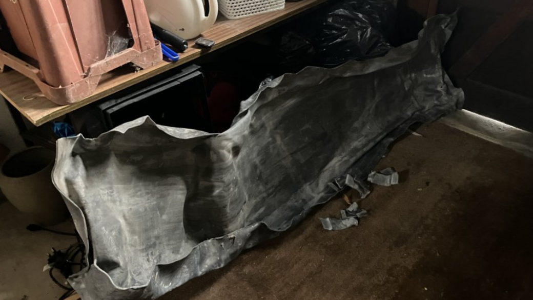 A large piece of roof lead lying on a floor in a small dark room