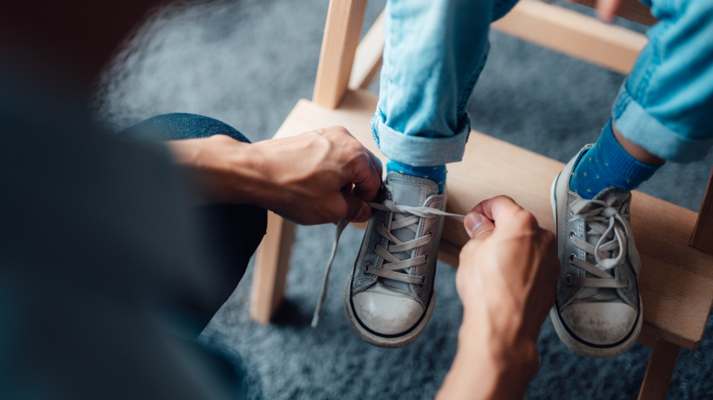 Man ties shoelaces of a young boy - we cannot see their faces