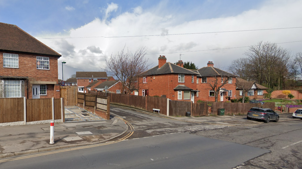 A traffic junction with houses and wooden fences either side.