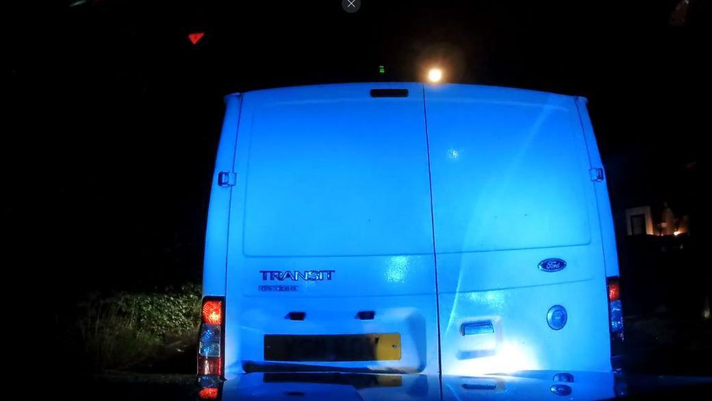 The back of a Ford Transit van illuminated by blue lights at night.