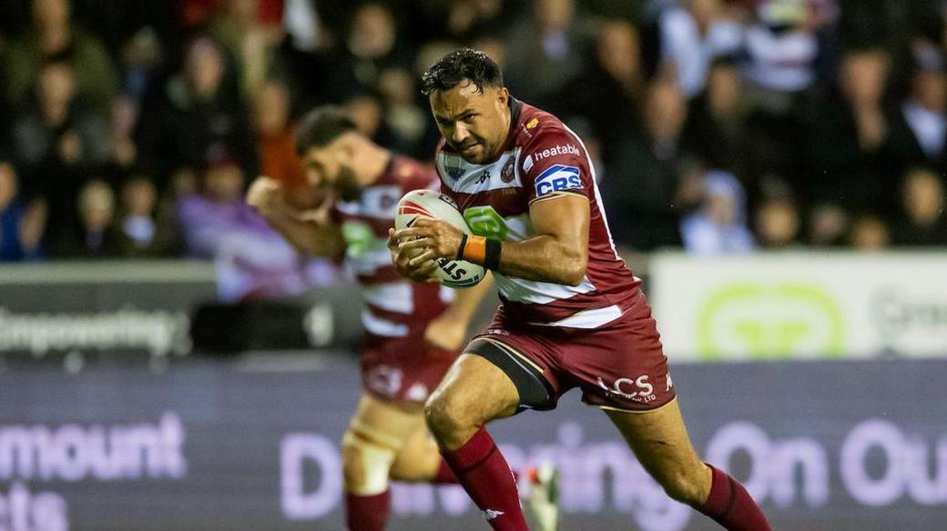 Wigan half-back Bevan French runs towards the try line as teammate Abbas Miski clenches his fist in celebration in the background.
