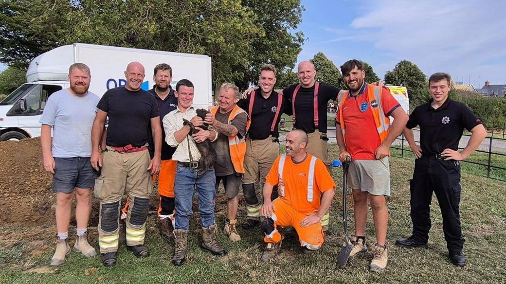 A group photo of the people involved in the rescue. In the middle is a man, who is Damsen's owner, holding the dog.