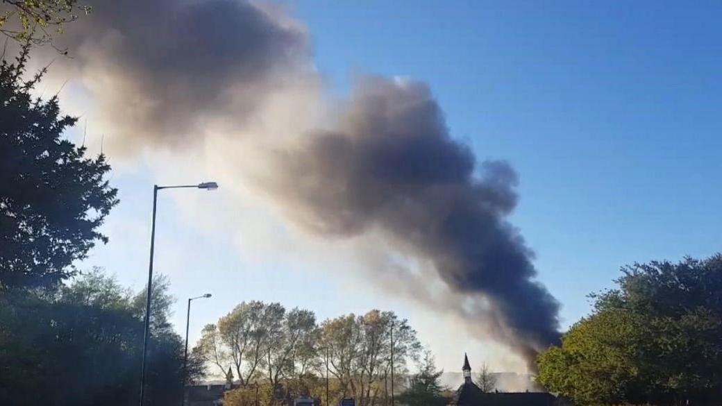 A plume of dark grey smoke towering in the blue sky above the  former Alex Smiles waste site in Sunderland.
