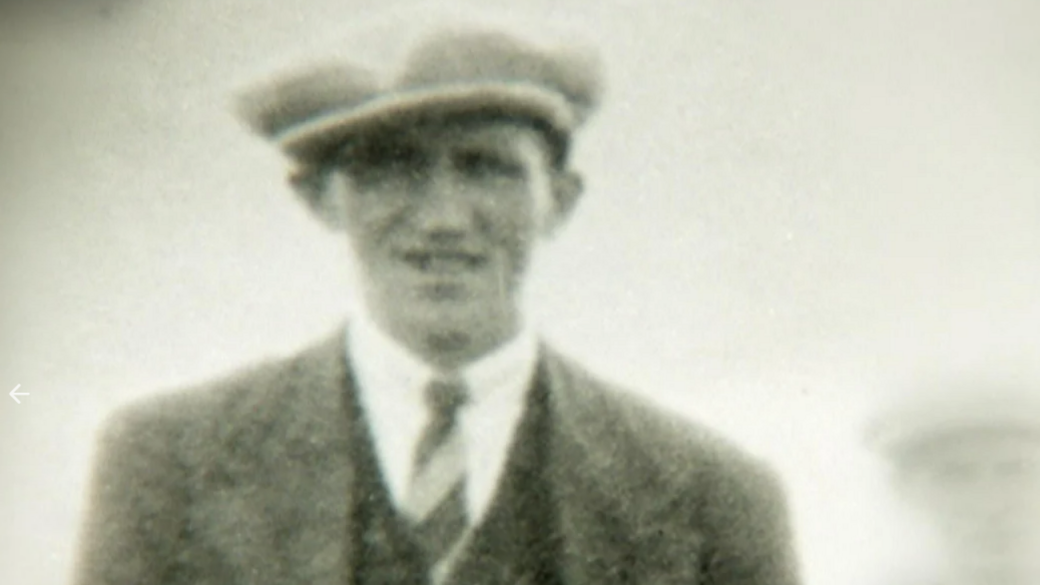 A black and white image of a young man with a suit, tie and cap on 