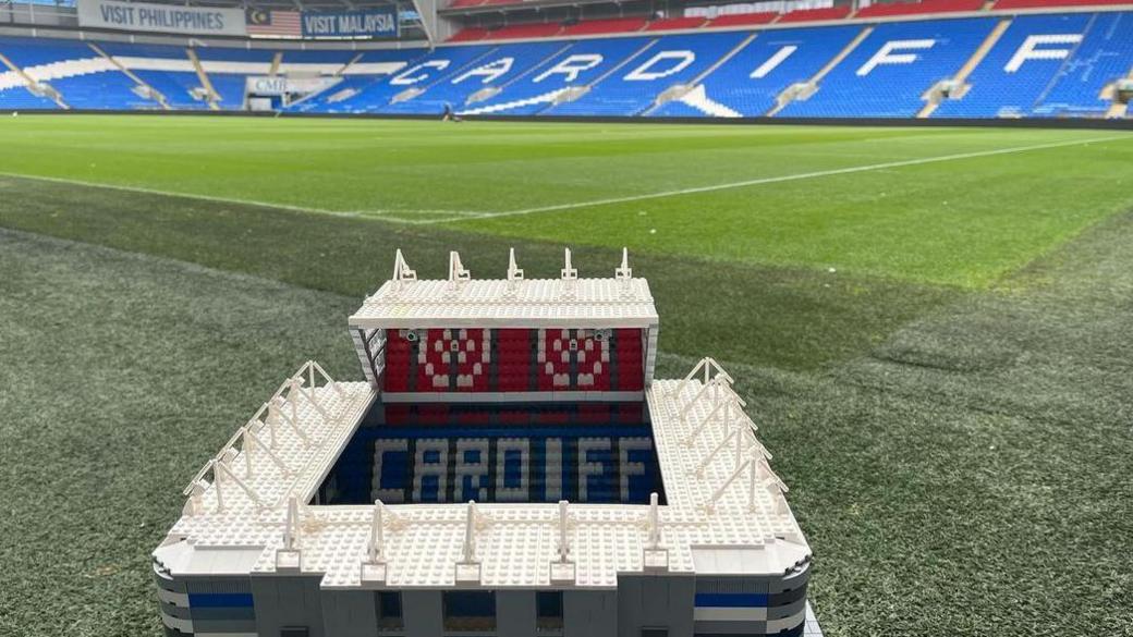 A Lego model of Cardiff City Stadium, sitting on the pitch of the actual stadium, with the stands in the background