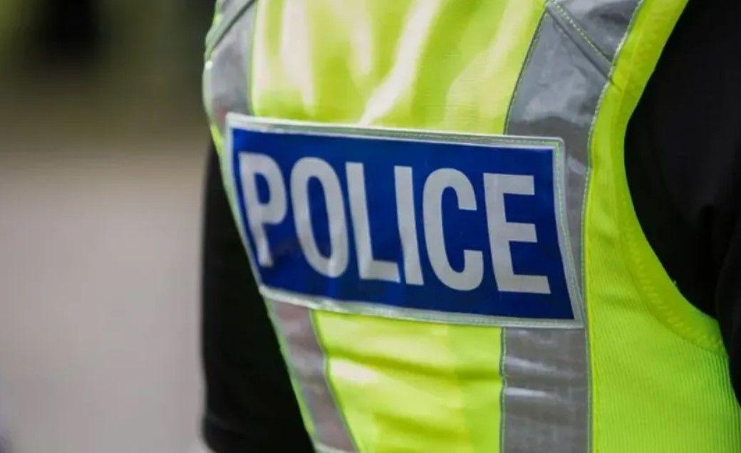 A close-up back view of a police officer wearing a high-visibility yellow jacket saying police in white letters on a blue background